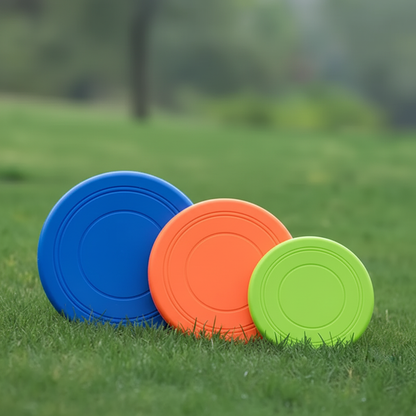 Three rubber dog frisbees in orange blue and green on grass outdoors
