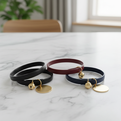Three cat collars in black burgundy and navy with gold bells on marble surface
